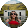 Woman in red swimsuit and sunglasses enjoying a natural hot spring pool in Iceland.