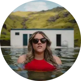 Woman in red swimsuit and sunglasses enjoying a natural hot spring pool in Iceland.