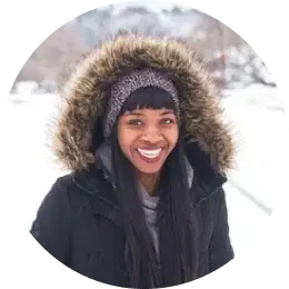 Smiling traveler bundled in a fur-lined hooded coat, enjoying Iceland's snowy landscape.