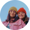 Two young women in colorful hats smiling outdoors.