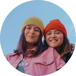 Two young women in colorful hats smiling outdoors.