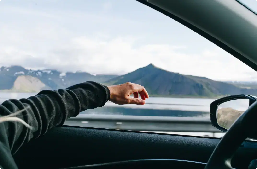 Hand reaching out of a car window while driving through scenic Icelandic landscapes, representing Cars Iceland’s reliable roadside assistance for a worry-free journey.