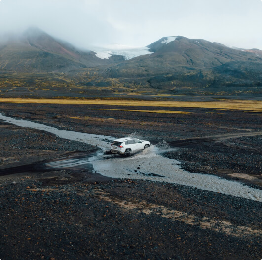 Land Rover Discovery parked in a rugged Icelandic landscape with red soil and rocky cliffs, showcasing the SUV's adventure-ready design under a bright blue sky.