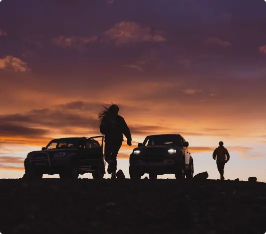 Silhouettes of people and two 4x4 SUVs set against a dramatic Icelandic sunset, emphasizing adventure and exploration on rugged terrain.