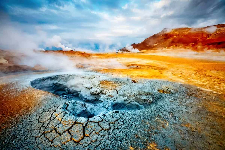 Vibrant geothermal area in Iceland with a steaming fumarole, colorful mineral deposits, and rugged landscape, showcasing the region's geothermal activity and unique geological features