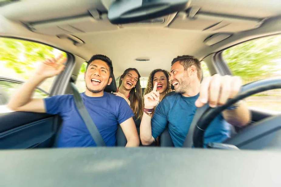 Four friends laughing and having a great time while driving in a car, enjoying each other's company.