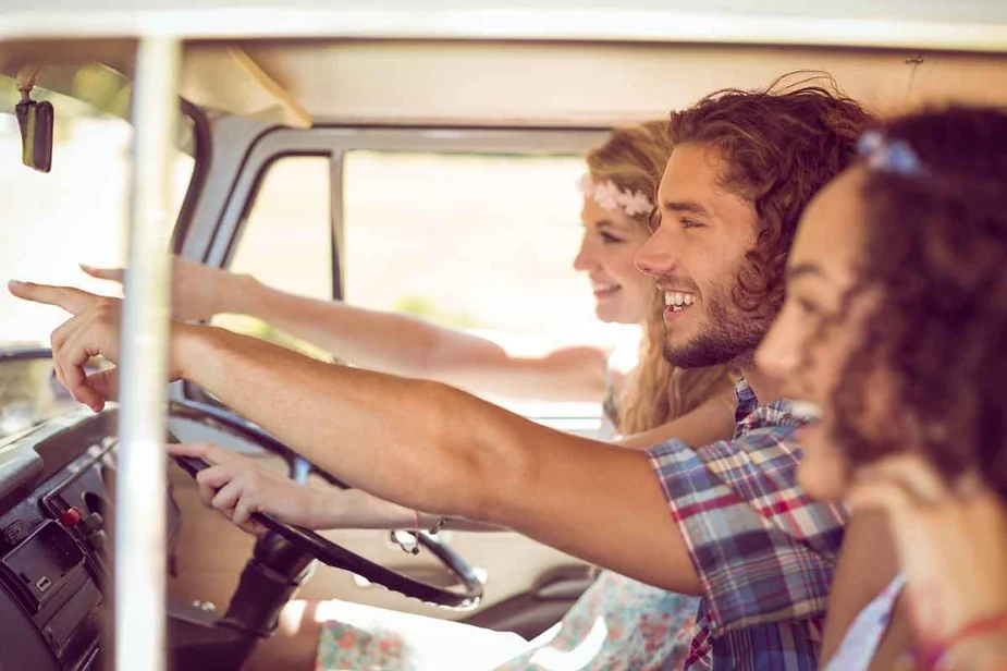 Three friends smiling and pointing out sights while driving in a car, enjoying a road trip together.