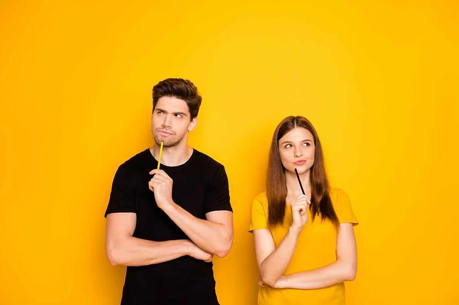 A young man and woman, each holding a pencil to their chin, appear thoughtful as they stand against a bright yellow background.