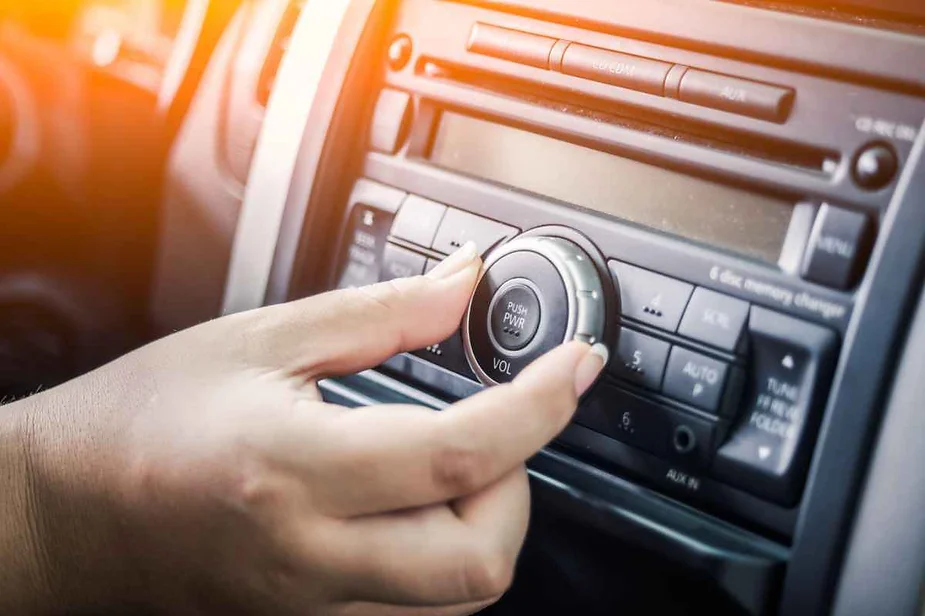 Close-up of a hand adjusting the volume knob on a car stereo system, with sunlight streaming in.