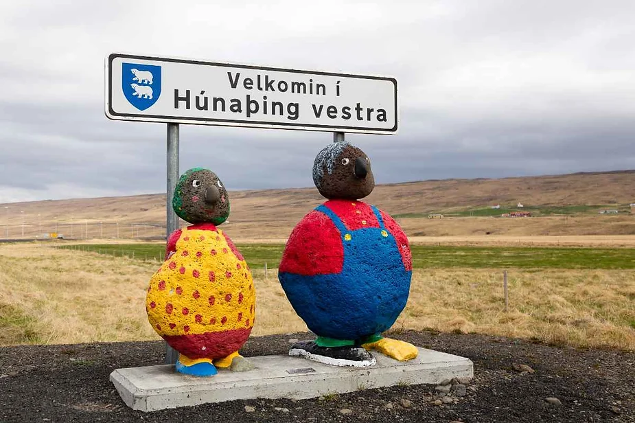 Colorful statues of two cartoon-like figures stand beside a welcome sign that reads 