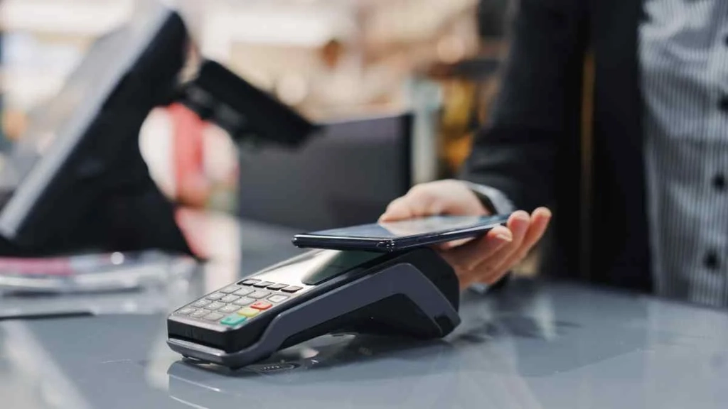 Close-up of a person using a smartphone to make a contactless payment at a card reader in Iceland, illustrating the convenience and technology of modern transactions.