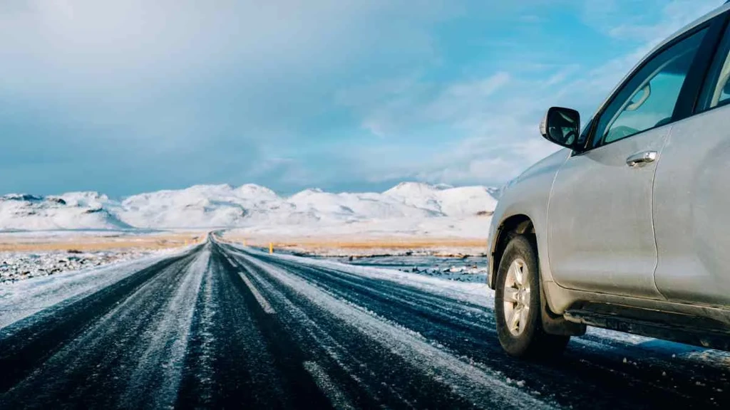 A car driving on a snow-covered road with a scenic view of snowy mountains in the background, representing the adventure and freedom of guided tours in Iceland.