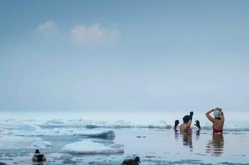 People in swimwear enjoying a dip in hot springs surrounded by snow and ice in Iceland during winter, illustrating the unique experience of geothermal bathing in frigid conditions.