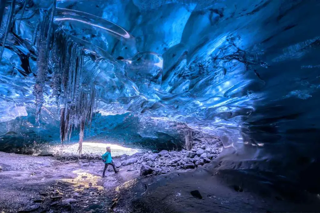 A person exploring a stunning blue ice cave with icicles hanging from the ceiling in Iceland, showcasing the breathtaking natural formations and the unique beauty of glacial caves.