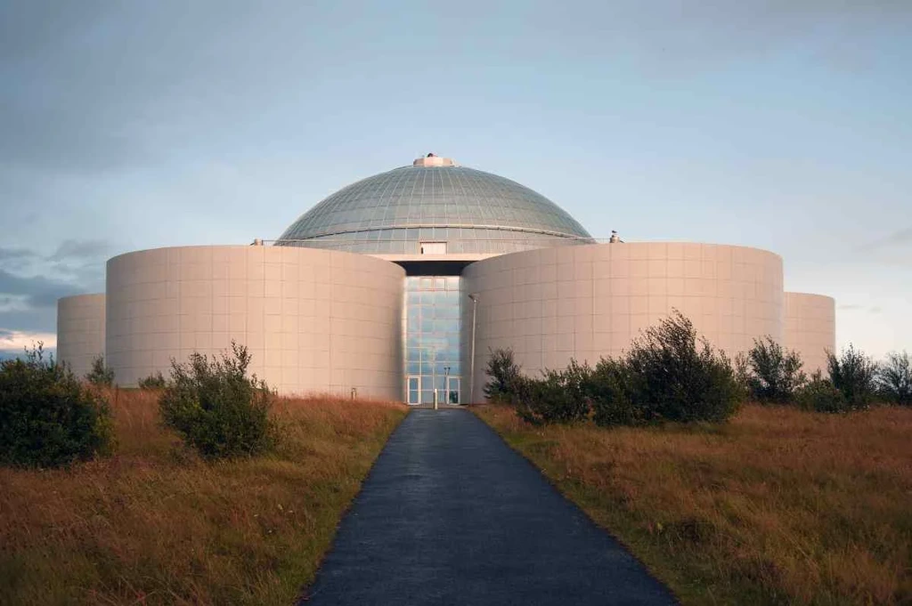 Modern dome-shaped building of the Perlan Museum in Iceland, surrounded by grass and bushes, showcasing its unique architecture and cultural significance.