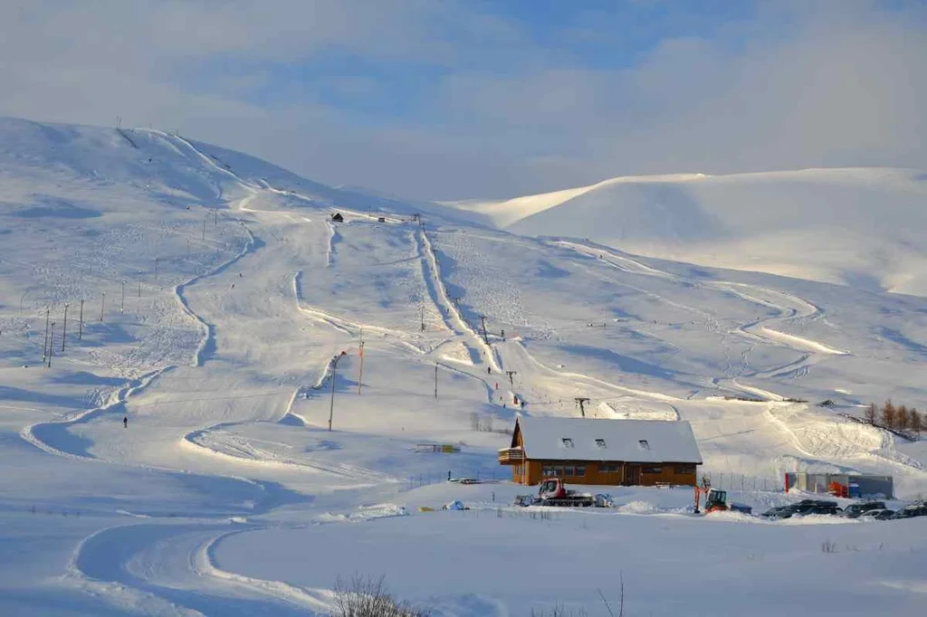 Snow-covered ski slopes and a wooden lodge under a clear blue sky in Iceland during winter, highlighting the recreational opportunities and serene beauty of the winter landscape.