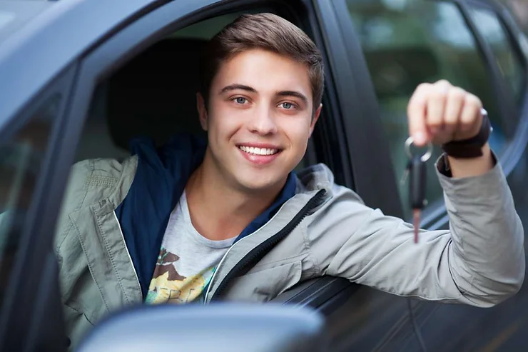 A smiling young man sitting in the driver's seat of a car, holding the car keys.