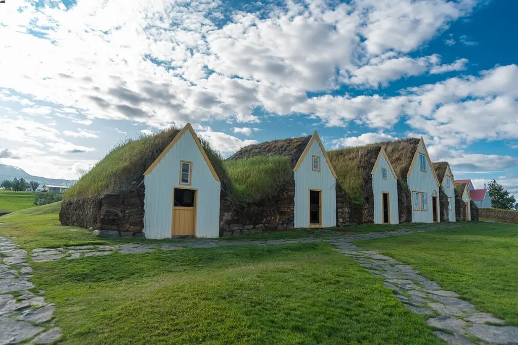 Traditional Icelandic turf houses at Glaumbaer, with grassy roofs and white wooden facades, under a partly cloudy sky, showcasing the historical and cultural heritage of Iceland.