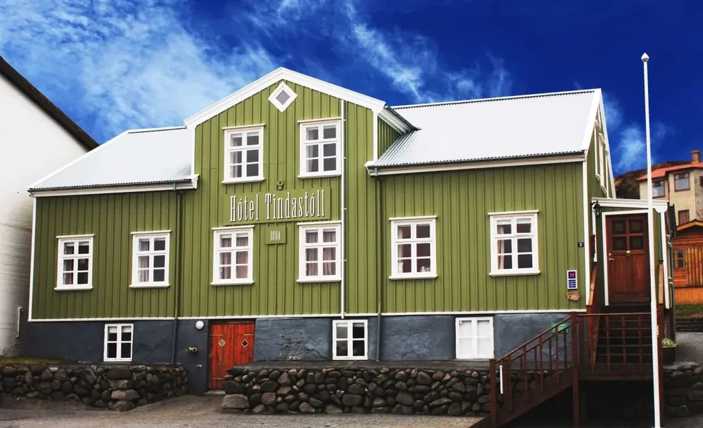 Historic green and white building of the Hótel Tindastóll, established in 1884, under a clear blue sky, showcasing its charming architecture and welcoming atmosphere.