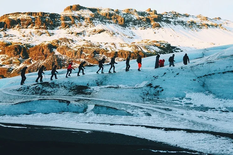 A group of hikers traversing the icy terrain of Vatnajökull Glacier in Iceland, with snow-capped mountains in the background.