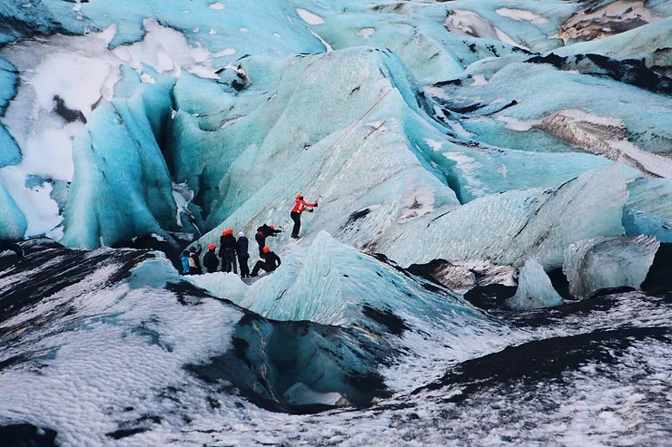 A group of hikers traversing the icy terrain of Solheimajokull Glacier in Iceland, highlighting the striking blue ice formations and the adventurous spirit of the trek.