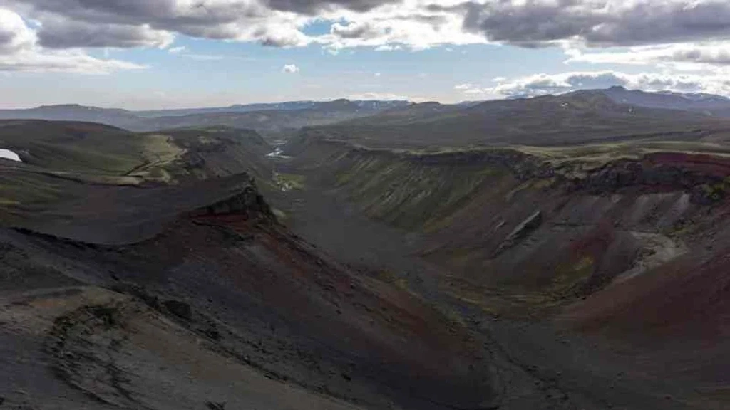 Panoramic view of the vast, rugged canyon landscape of Eldgjá in Iceland, under a partly cloudy sky, showcasing the dramatic geological formations and natural beauty.