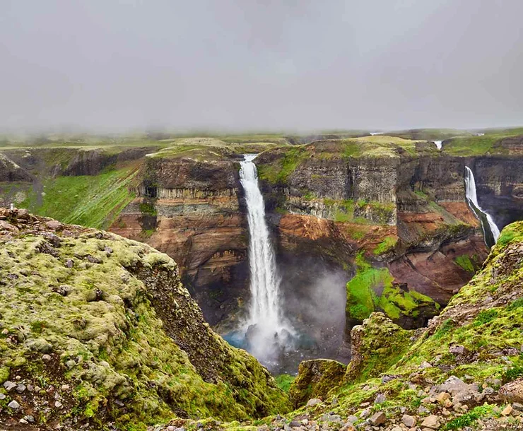 The breathtaking Haifoss Waterfall in Iceland plunges dramatically over a rugged cliff, surrounded by lush green moss and rocky terrain, creating a mesmerizing natural scene.