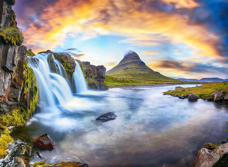 Kirkjufellsfoss Waterfall in Iceland, showcasing a picturesque cascade flowing over rocky cliffs into a tranquil stream, with the iconic Kirkjufell mountain in the background under a dramatic, colorful sky at sunset.