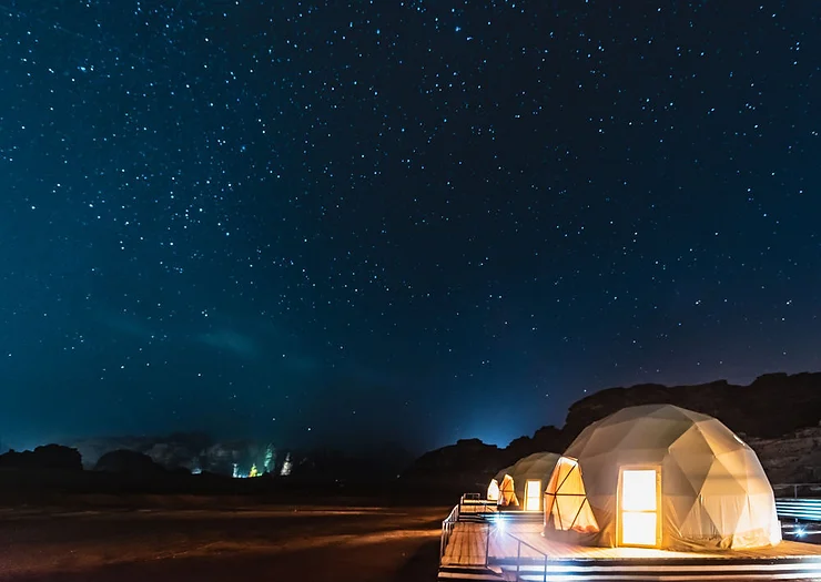 A night view of dome-shaped hotel rooms illuminated from within, set against a stunning backdrop of a starry sky in Iceland. The clear night sky is filled with countless stars, creating a magical and serene atmosphere. The unique dome structures are situated in a remote location, offering a perfect blend of comfort and nature's beauty.