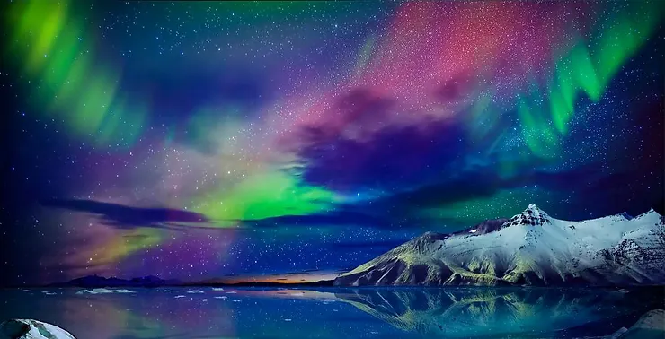 A breathtaking display of the Northern Lights with vibrant green and purple hues illuminating the night sky over snow-covered mountains and a calm, reflective lake in Iceland.