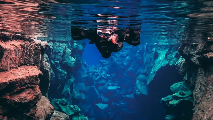 A snorkeler in a wetsuit exploring the crystal-clear waters of the Silfra Fissure in Iceland, surrounded by dramatic rock formations.