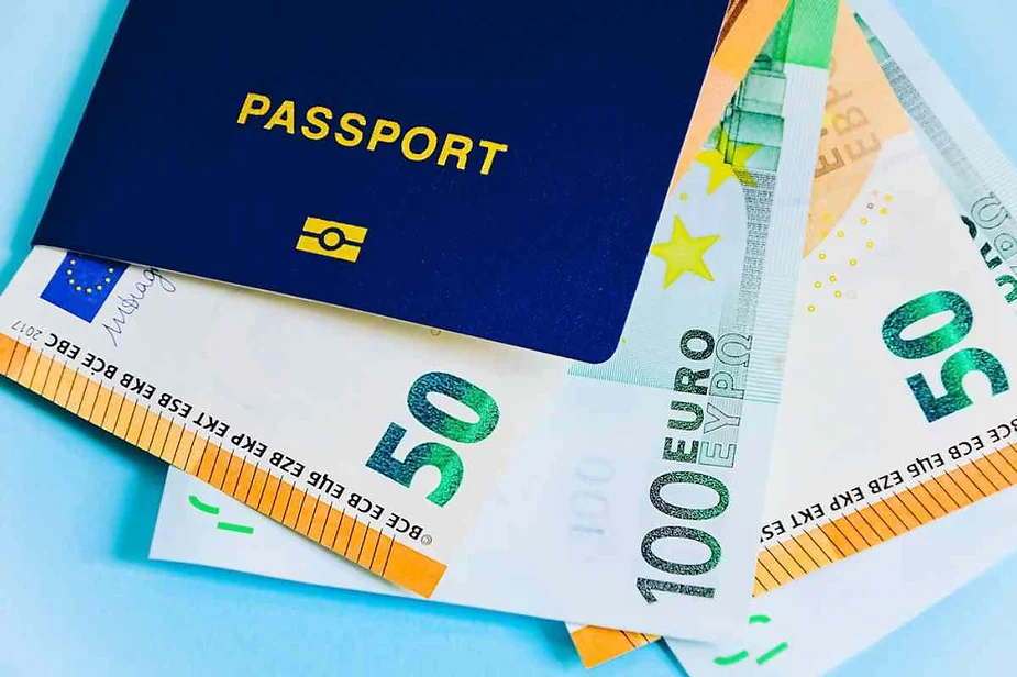 A blue passport placed over several Euro banknotes, including denominations of 50 and 100 Euros. The scene suggests travel preparations or financial readiness for a trip.