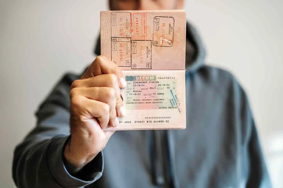 A person holding up an open passport with multiple visa stamps and a visible visa page.