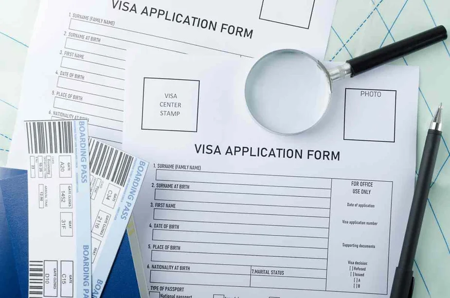 Visa application forms with boarding passes, a magnifying glass, and a pen on a table.