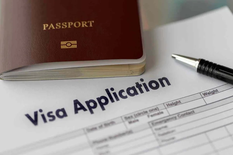 A close-up image of a visa application form with a pen and a passport placed on top of it.