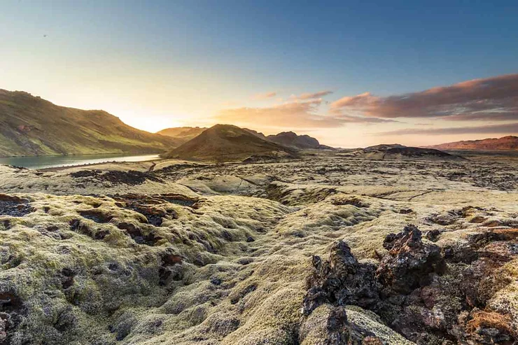 A scenic view of the Reykjanes Peninsula in Iceland, showcasing the unique moss-covered lava fields with mountains in the background and a beautiful sunrise or sunset.