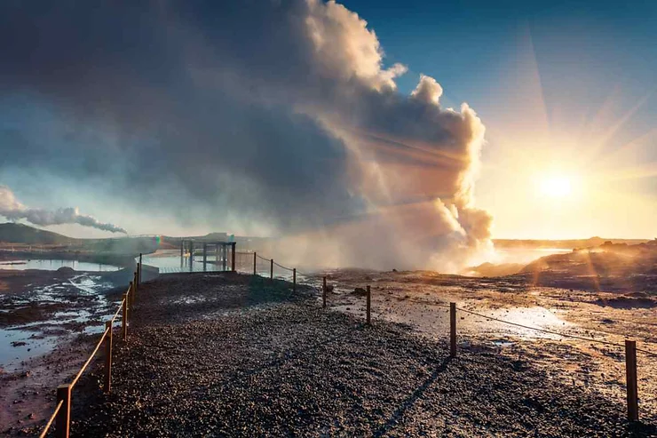 A captivating view of a geothermal area in Reykjanes Peninsula, Iceland, featuring steam rising from the hot springs against a backdrop of a vibrant sunrise or sunset.