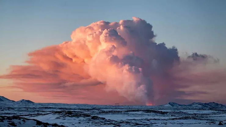 A breathtaking view of a massive cloud formation with a pinkish hue during sunset over the snowy landscape of the Reykjanes Peninsula Nature Reserve in Iceland.