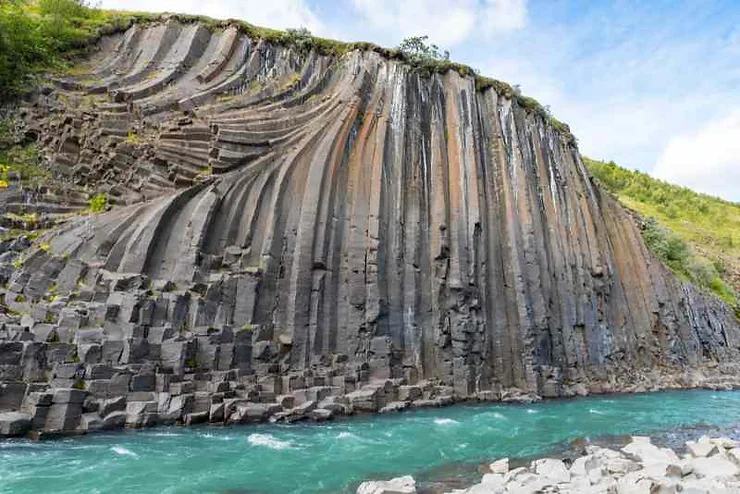 A close-up view of the basalt columns in Studlagil Canyon, Iceland, displaying the unique, curved formations above a vibrant turquoise river.