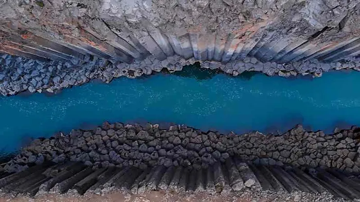 An aerial view of the turquoise river running through Studlagil Canyon, Iceland, showcasing the striking vertical basalt columns on either side.