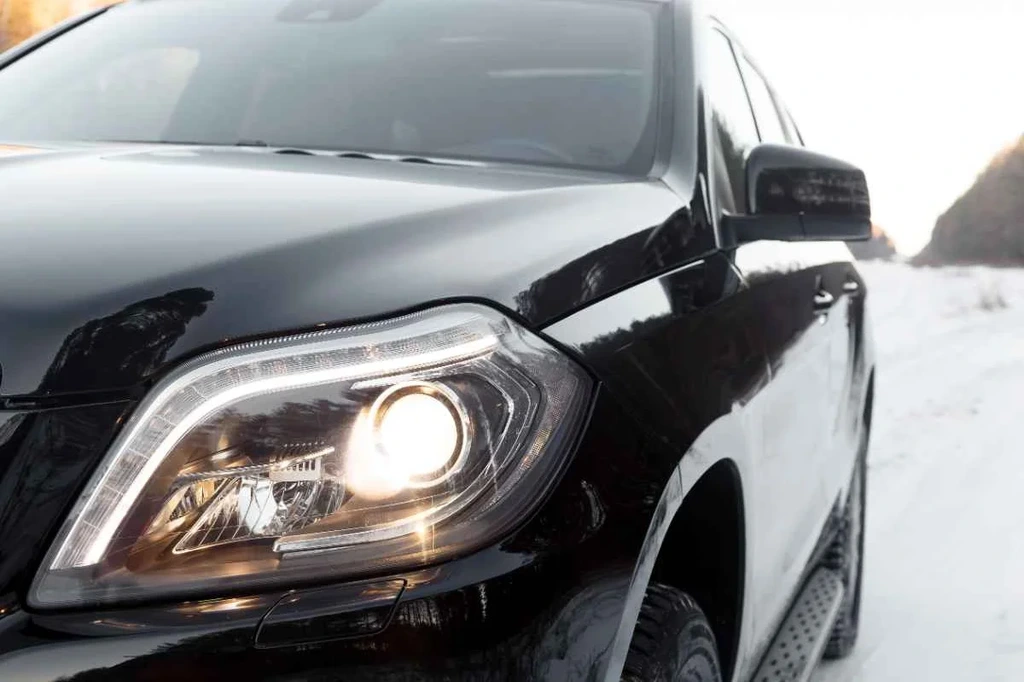 A close-up of a black SUV with its headlights on during winter, reflecting the snow-covered surroundings.