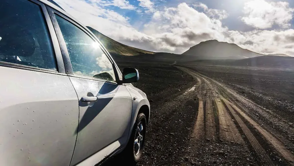 A white SUV parked on a gravel road in the Icelandic wilderness with rugged mountains in the background.