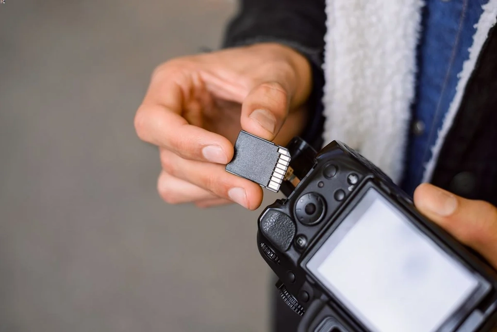 Close-up of a person inserting an extra memory card into a camera, highlighting the importance of carrying additional storage for capturing moments during travels.