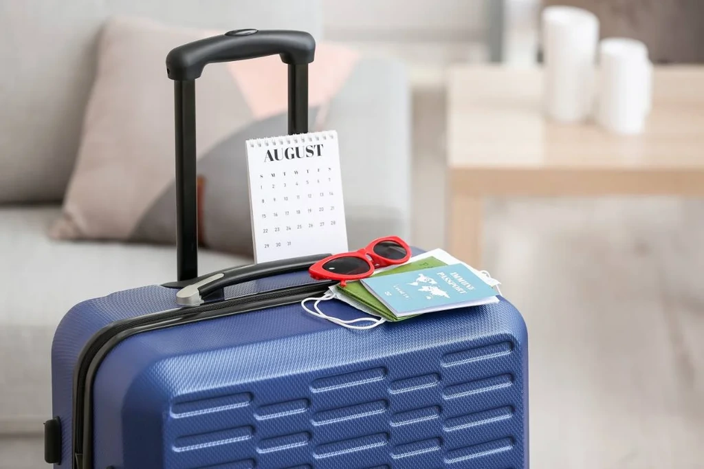 Close-up of a blue suitcase with a calendar marked August, sunglasses, and a passport ready for trip