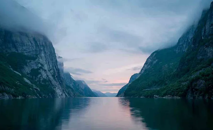 A serene fjord in Iceland with towering cliffs shrouded in mist and calm waters reflecting the soft light of the sky.