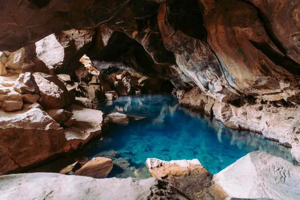 Blue thermal spring inside Grjotagja Cave in Iceland, surrounded by rugged rock formations.