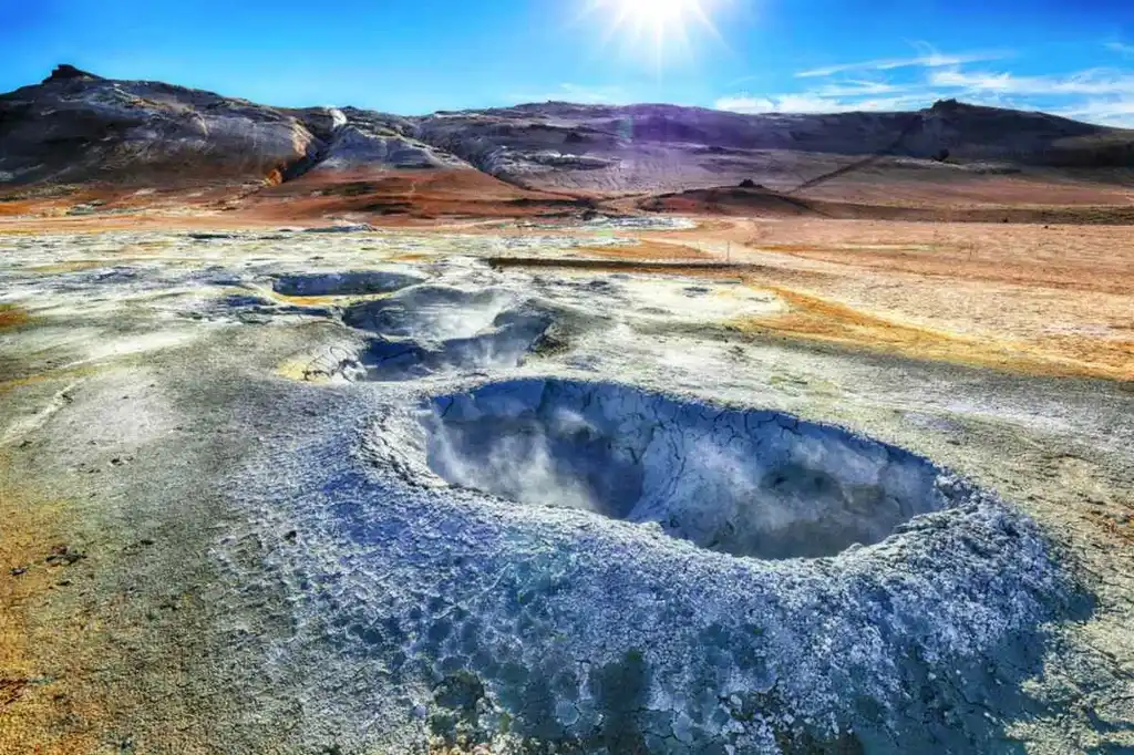 Hverir geothermal area in North Iceland with bubbling mud pots and steaming fumaroles under a bright blue sky.