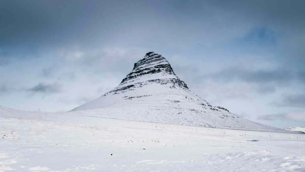 Snow-covered Kirkjufell mountain under a cloudy sky in Iceland during winter.