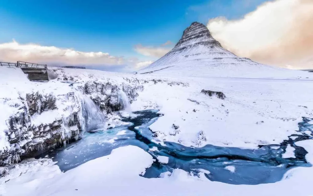 Kirkjufell Mountain, a uniquely shaped peak in Iceland, surrounded by lush green landscapes and blue sky.