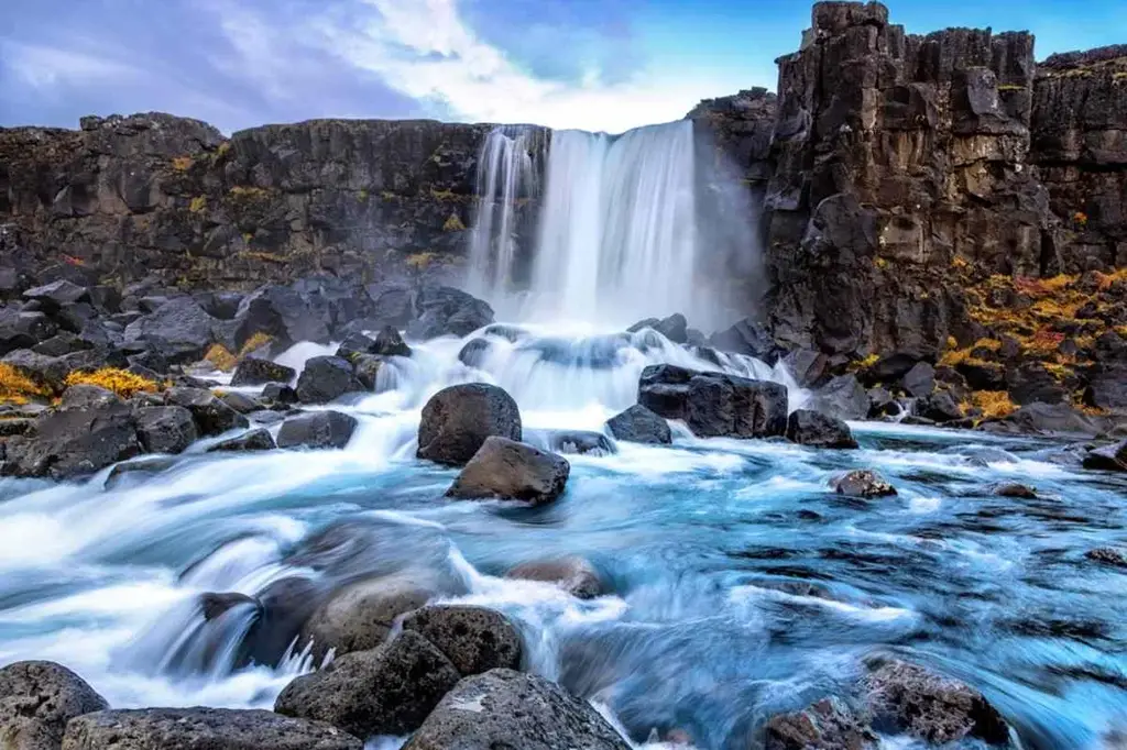 Oxararfoss waterfall in Thingvellir National Park, Iceland, cascading over rocky cliffs into a vibrant blue stream.